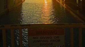 A sunset over a waterway between buildings with a warning sign about no diving or jumping from the bridge. - JB City Shopping Mall Apartment (Johor Bahru)