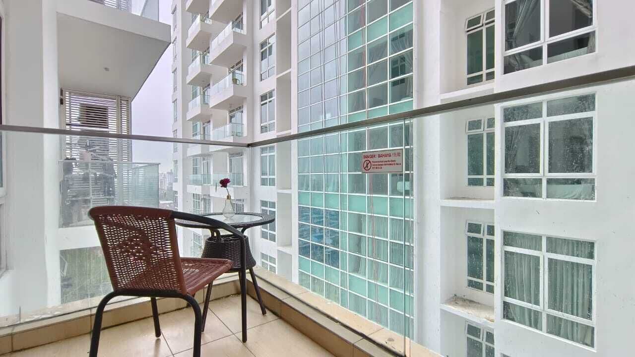A balcony with a glass railing, a wicker chair, and a small table with a vase of flowers.
