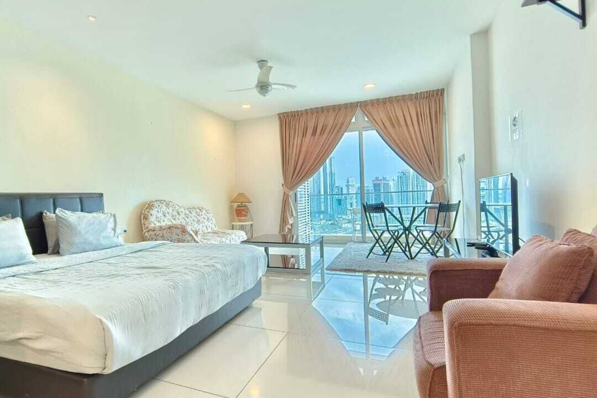 A modern hotel room with a large bed, a dining area with a glass table, and a view of the cityscape.