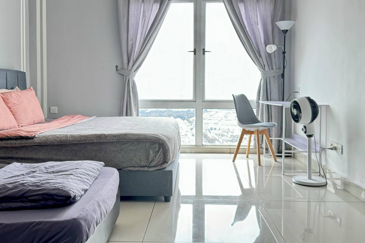 A modern bedroom with a bed, a chair, a desk, and a standing fan.