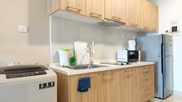 A modern kitchen with wooden cabinets, a stainless steel refrigerator, a coffee maker, and a washing machine.