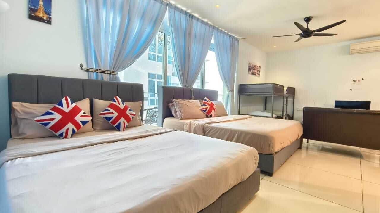 A hotel room with two beds, a desk, a ceiling fan, and large windows with curtains.