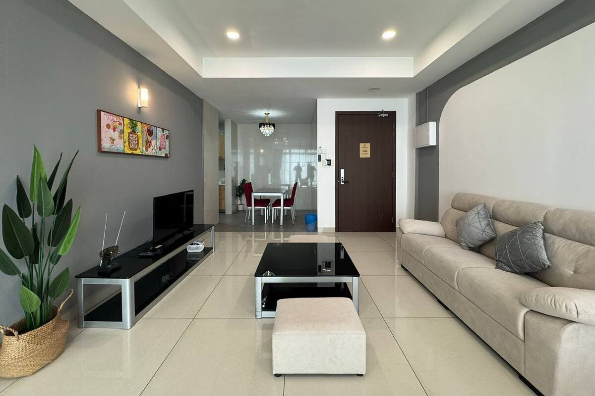 A modern living room with a sofa, a coffee table, a TV, and a dining area in the background.