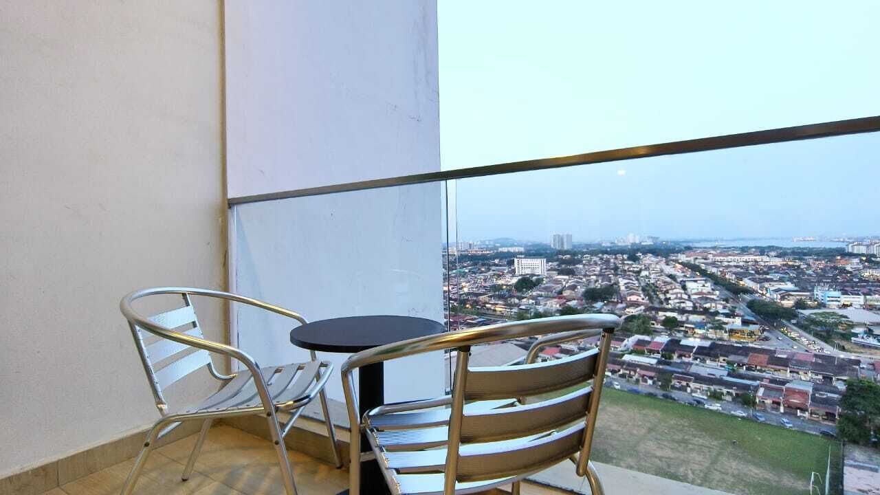 En balkon med to metalstole og et lille bord, med udsigt over et bybillede med bygninger og veje.