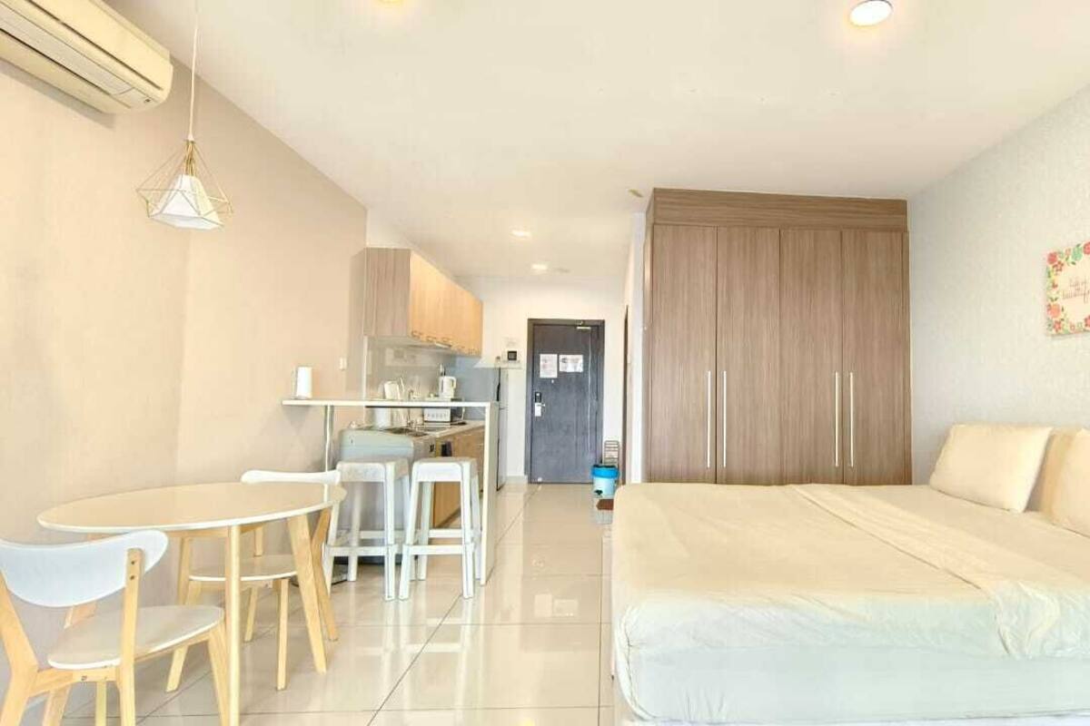 A modern hotel room with a bed, a dining table with chairs, a kitchenette, and a large wardrobe.