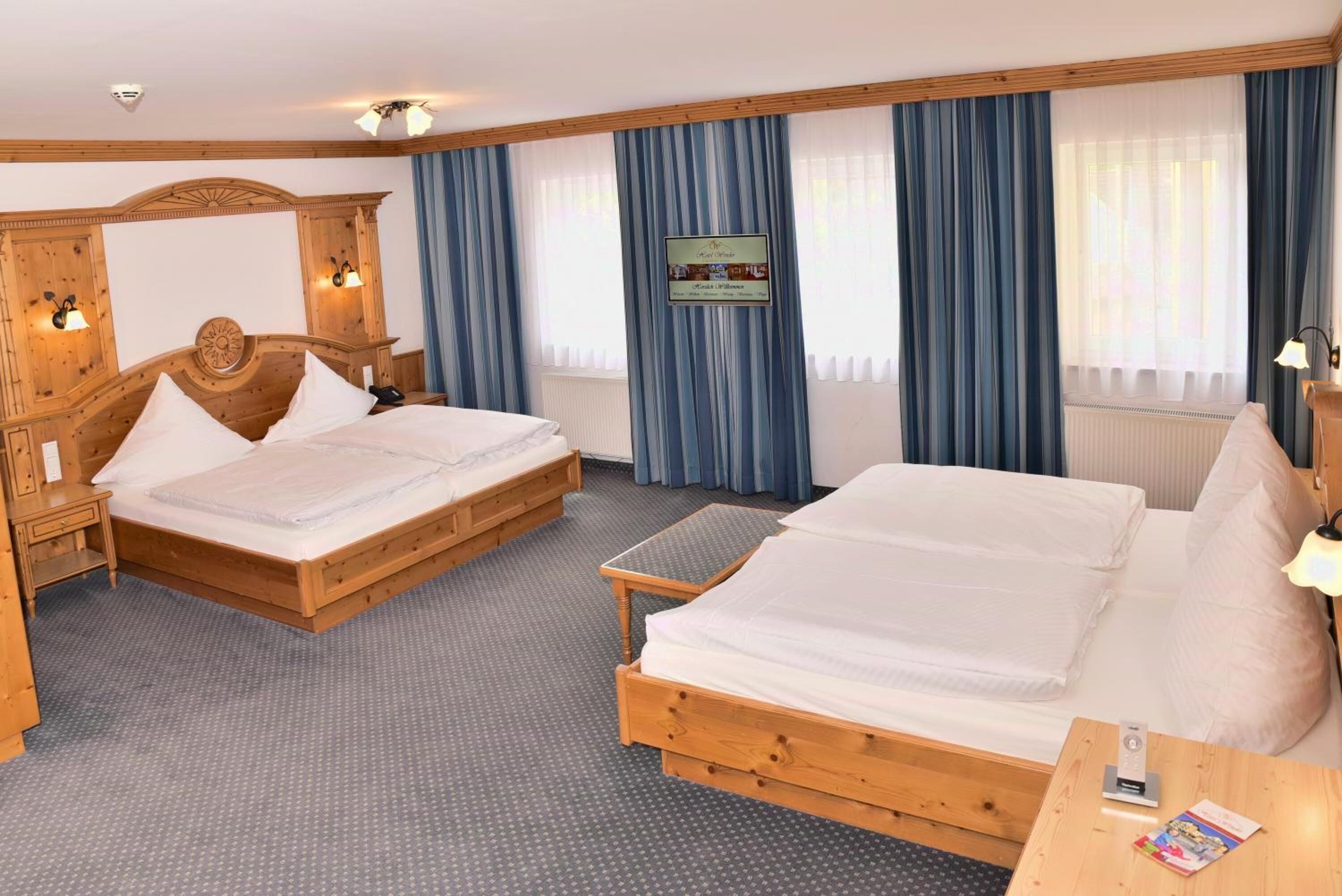 Een hotelkamer met twee houten bedden, een nachtkastje van hout, een klein tafeltje en een tv aan de muur.