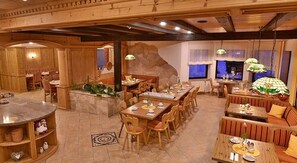 A restaurant with wooden furniture, a stone island, and hanging lamps. - Hotel Wender (Aurach)