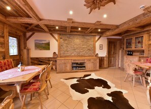 A rustic interior with exposed wooden beams, a stone fireplace, a dining area with wooden furniture, and a cowhide rug. - Hotel Wender (Aurach)