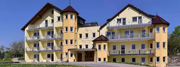 A multi-story hotel with balconies, a central entrance, and a clear sky. - Hotel Wender (Aurach)