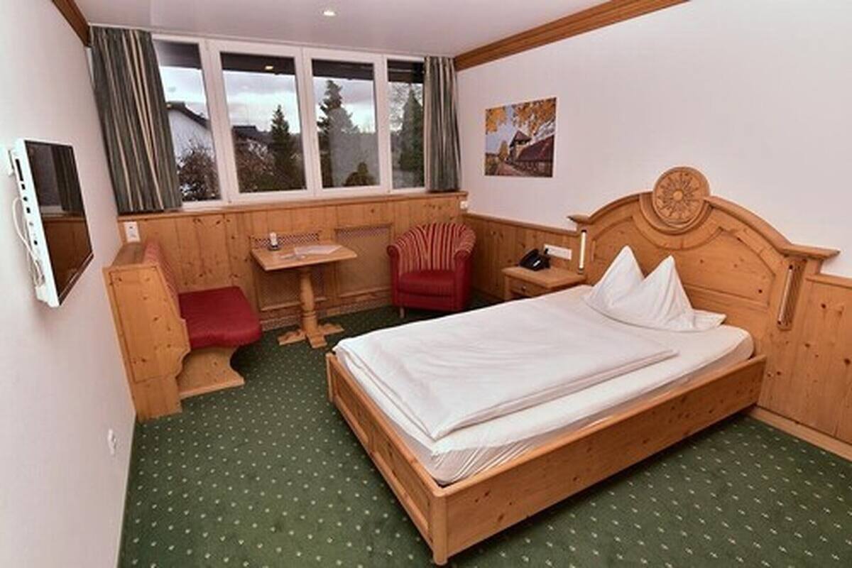 A wooden bed with white linens, a wooden desk, a red chair, and a window with curtains.