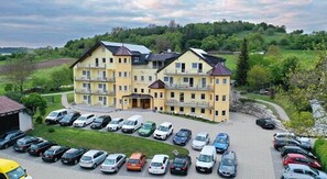 A multi-story hotel with a central entrance, multiple balconies, and a parking lot filled with cars. - Hotel Wender (Aurach)