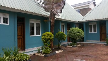 Un edificio con fachada azul, ventanas blancas y tejado de tejas. Hay tres árboles pequeños en frente.