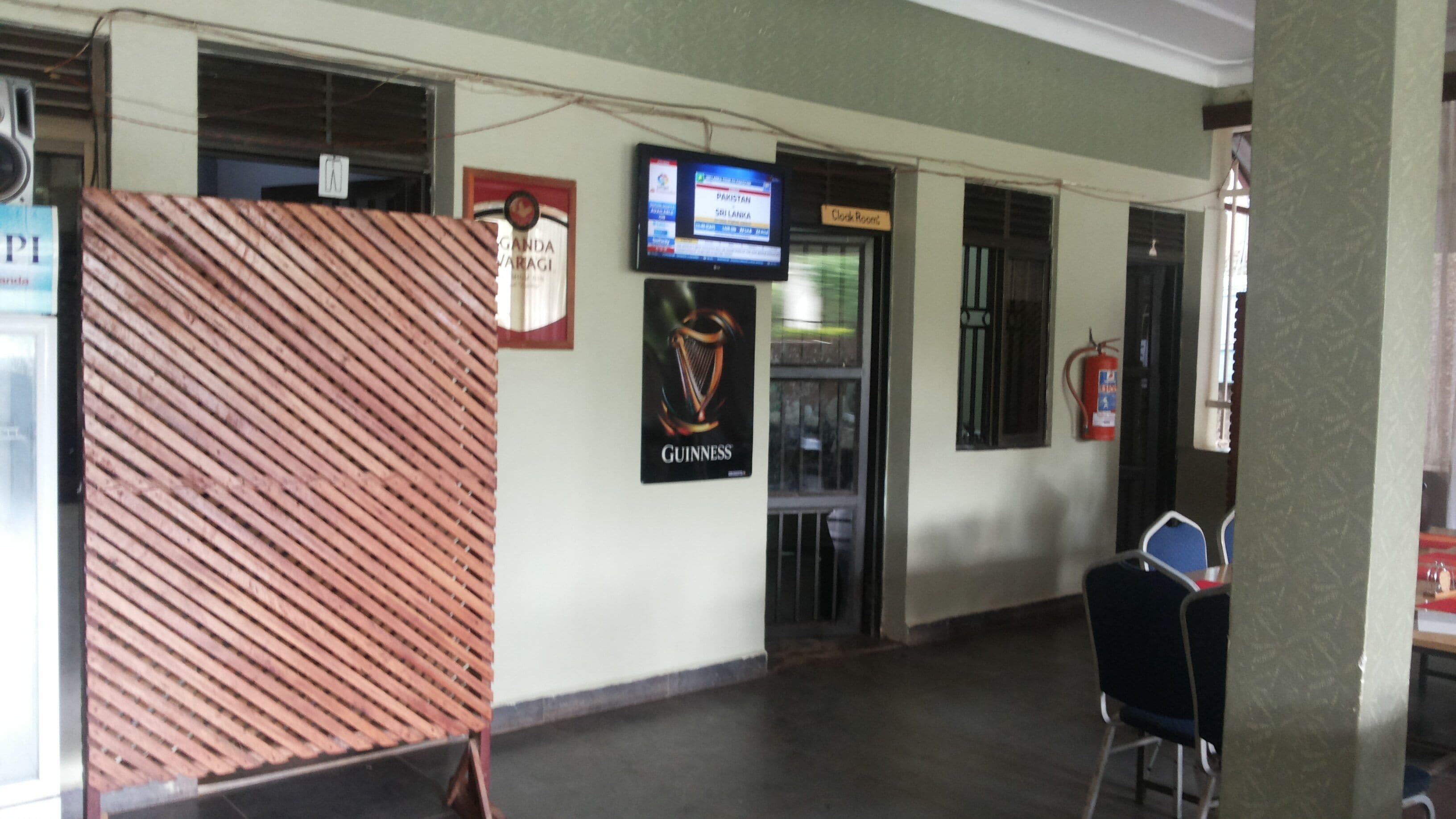 A hallway with a wooden partition, a television screen displaying a news channel, a sign for a clock room, and a fire extinguisher on the wall.