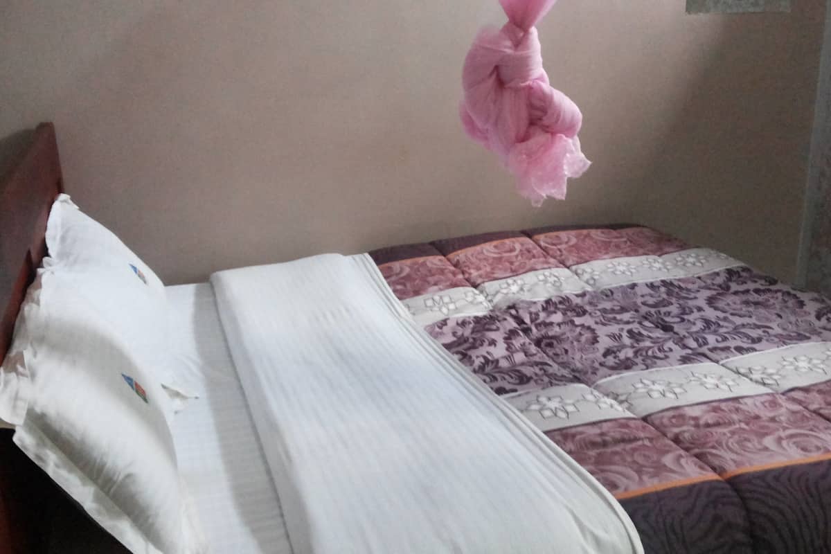 A bed with a white and patterned bedspread, a wooden headboard, and a pink hanging decoration.