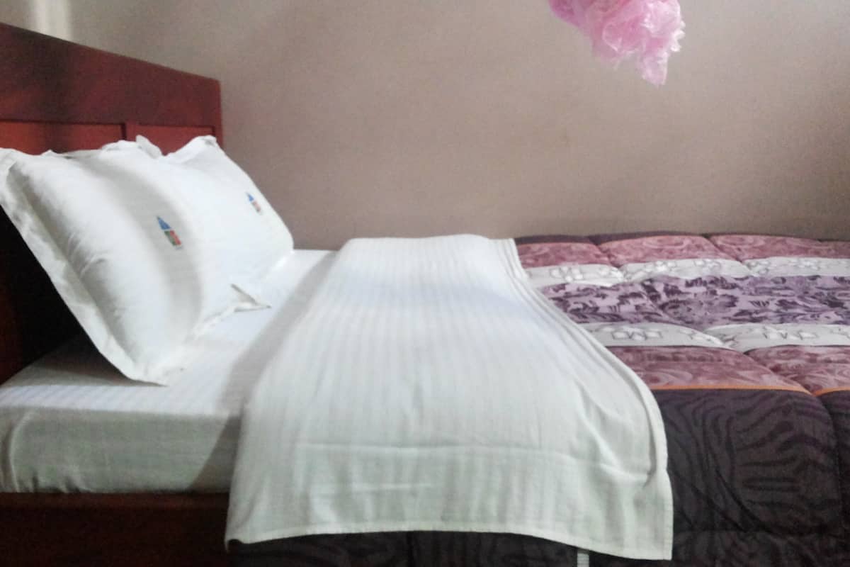 A bed with a white bedspread and pillows, a wooden headboard, and a patterned blanket.