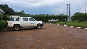 Una camioneta pickup blanca estacionada en un camino de ladrillo mojado, con follaje verde y un cielo despejado al fondo.