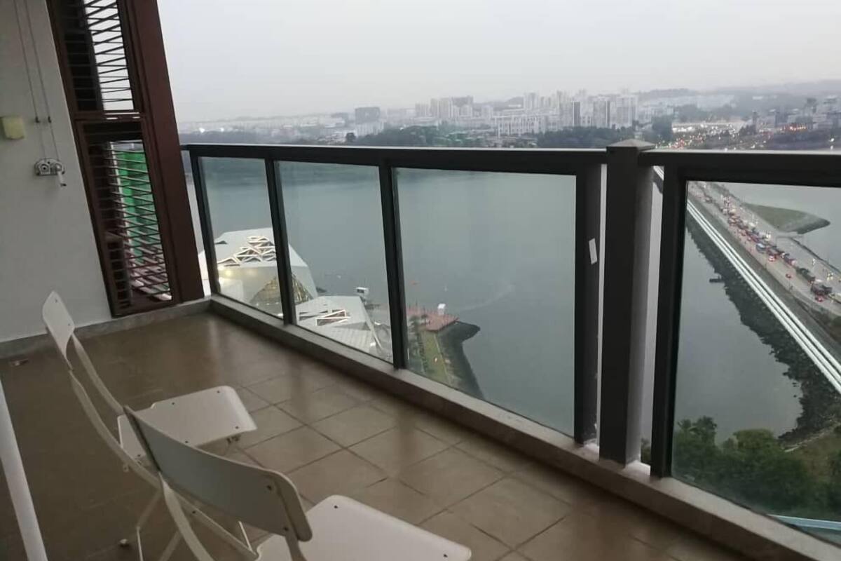 Ein Balkon mit Blick auf einen Fluss und eine Stadtansicht. Auf dem Boden stehen zwei weiße Stühle.