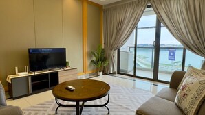 Une chambre d’hôtel moderne dotée d’un grand téléviseur à écran plat, d’une table basse ronde, d’un canapé et offrant une vue sur la mer grâce à de grandes fenêtres.