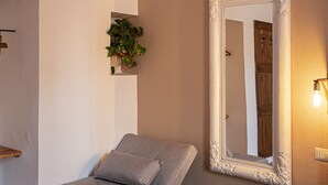 Un dormitorio pequeño y moderno con un sofá cama gris, un espejo grande y un taburete de madera.