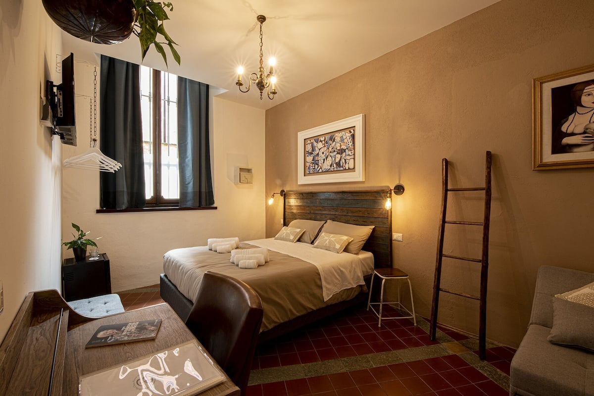 A bedroom with a bed, bedside table, lamp, and a painting on the wall.