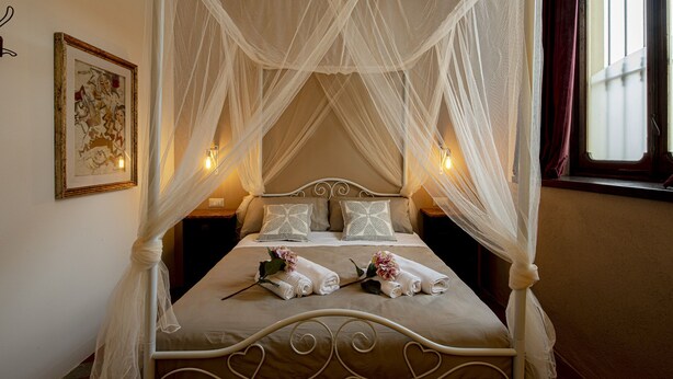 Una cama con dosel y cuatro columnas con ropa blanca y detalles con forma de corazón en el cabecero.