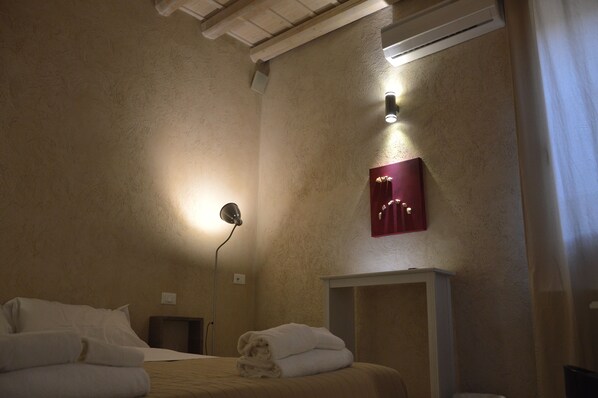A hotel room with a bed, a bedside table, a lamp, a wall-mounted light, and a red decorative panel.