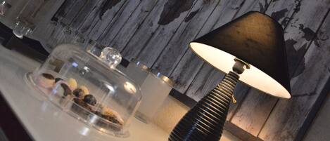 A lamp with a black shade on a table, a glass container with food items, and a wooden wall with a distressed finish.