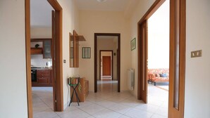 A hallway with a kitchen area on the left, a living room with a sofa and a radiator on the right, and a door leading to another room. - B&B San Francesco (Nicosia)