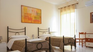 A hotel room with two single beds, a wooden dresser, a painting on the wall, and a window with curtains. - B&B San Francesco (Nicosia)