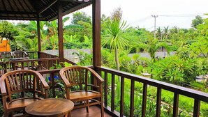 A wooden deck with chairs and a table, surrounded by lush greenery and a view of a garden. - Dream Beach Berlian (Lembongan Island)