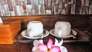 Two white ceramic cups on saucers on a wooden tray, with a pink orchid flower in front. - Dream Beach Berlian (Lembongan Island)