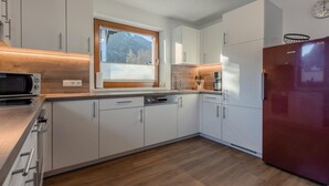 A modern kitchen with white cabinets, a wooden countertop, a built-in microwave, a red refrigerator, and a window with a mountain view. - Spacious apartment for up to 9 people with garden (Umhausen)