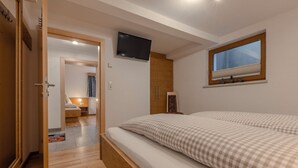 A bedroom with a bed, a TV mounted on the wall, a window, and a door leading to another room. - Spacious apartment for up to 9 people with garden (Umhausen)