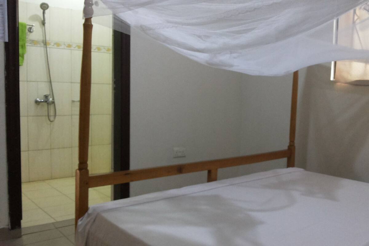 A single bed with a wooden frame and white bedding in a room with a tiled shower area.
