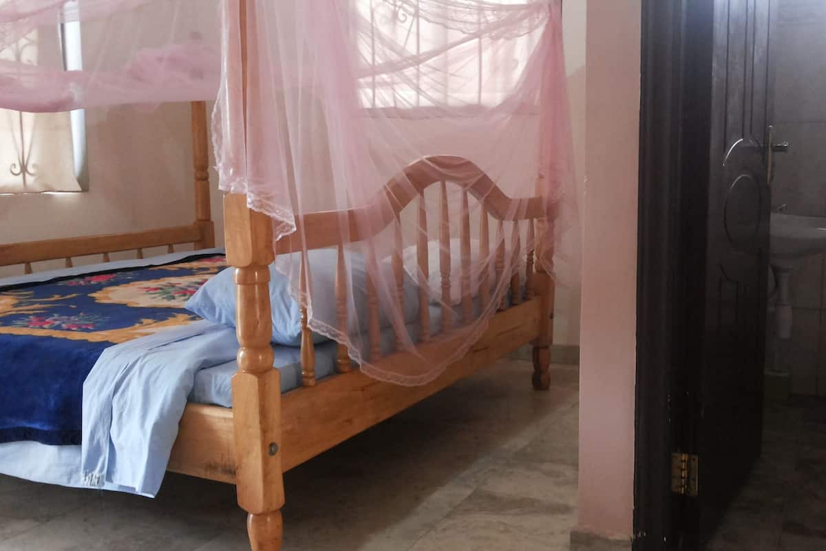 A bedroom with a wooden bed, a mosquito net, and a bathroom with a toilet and sink.