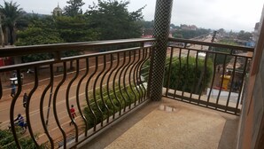 A balcony with a view of a busy street, a metal railing, and a checkered pattern on the wall. - Highway Motel (Nebbi)