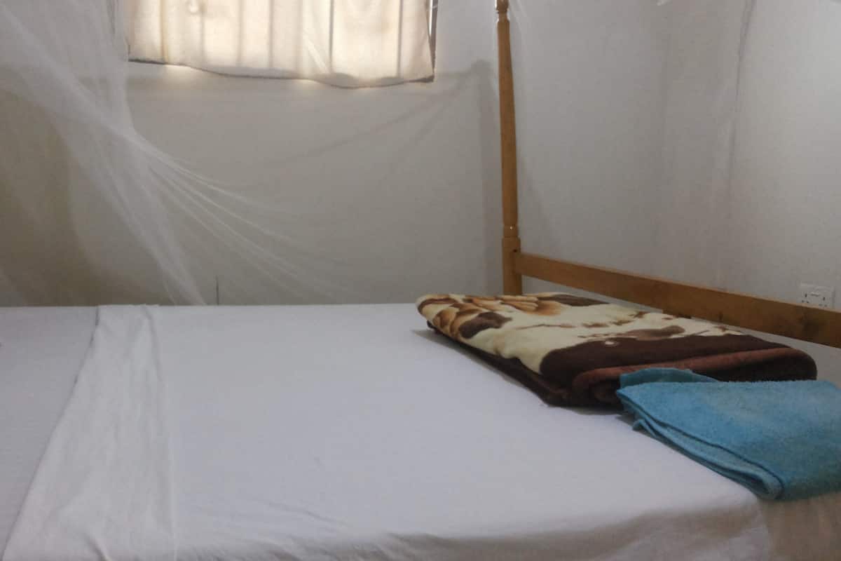 A single bed with a white mattress, a brown and white patterned blanket, and a blue towel.