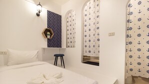 A hotel room with a large bed, a small stool, a wall-mounted shelf with a plant, and curtains with an anchor pattern.