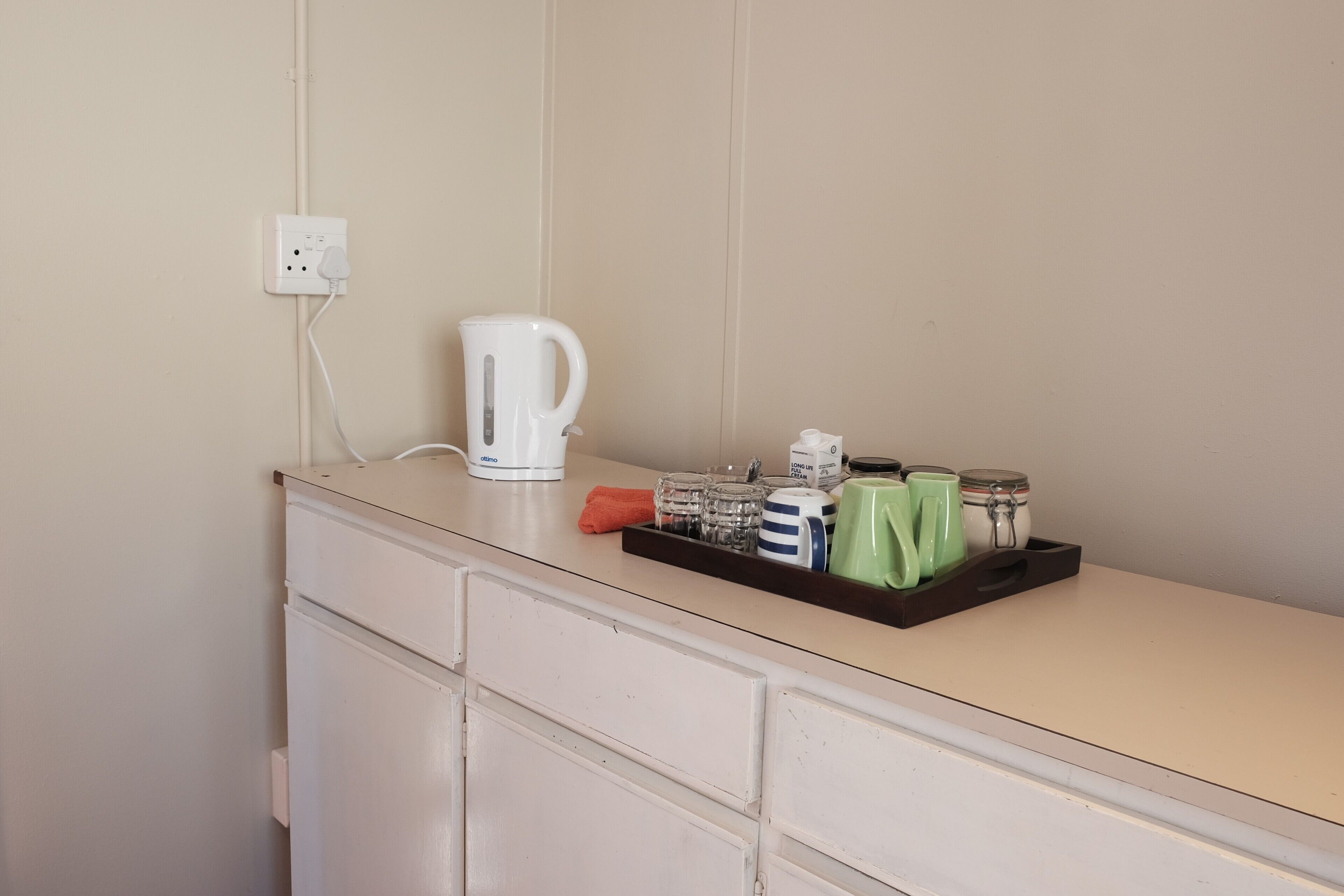 Une petite cuisine équipée d’une bouilloire blanche, d’un plateau avec des bocaux et d’une machine à café.