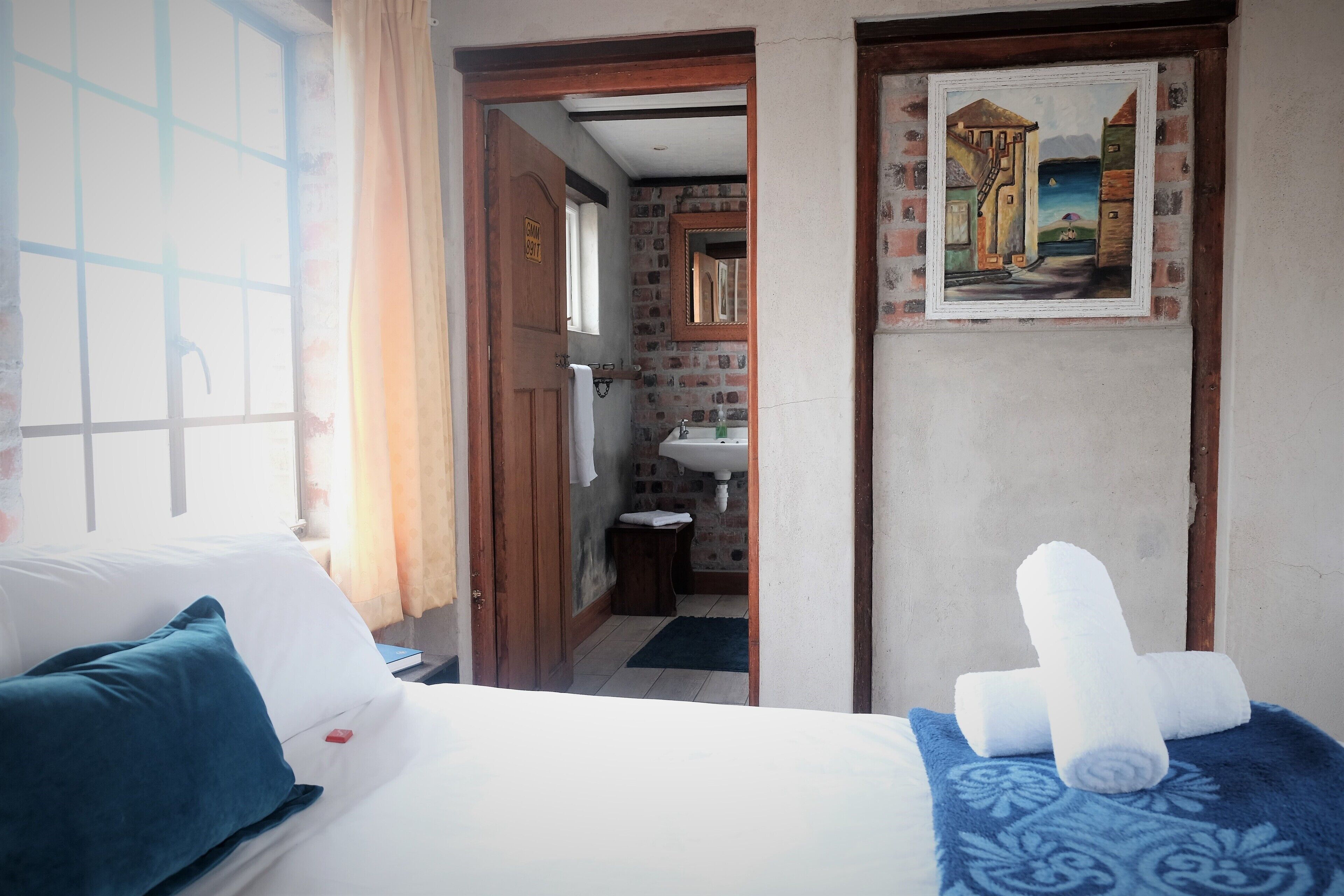 A hotel room with a bed, a bathroom visible through an open door, and a painting on the wall.