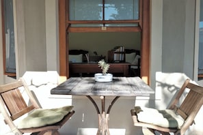 A wooden table with a potted plant, two wooden chairs with cushions, and a view of a room with a desk and books. - The Yard - Hostel (Cape Town)