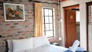 Une chambre d’hôtel avec un lit, un tableau au mur, une fenêtre avec des rideaux et une porte en bois.