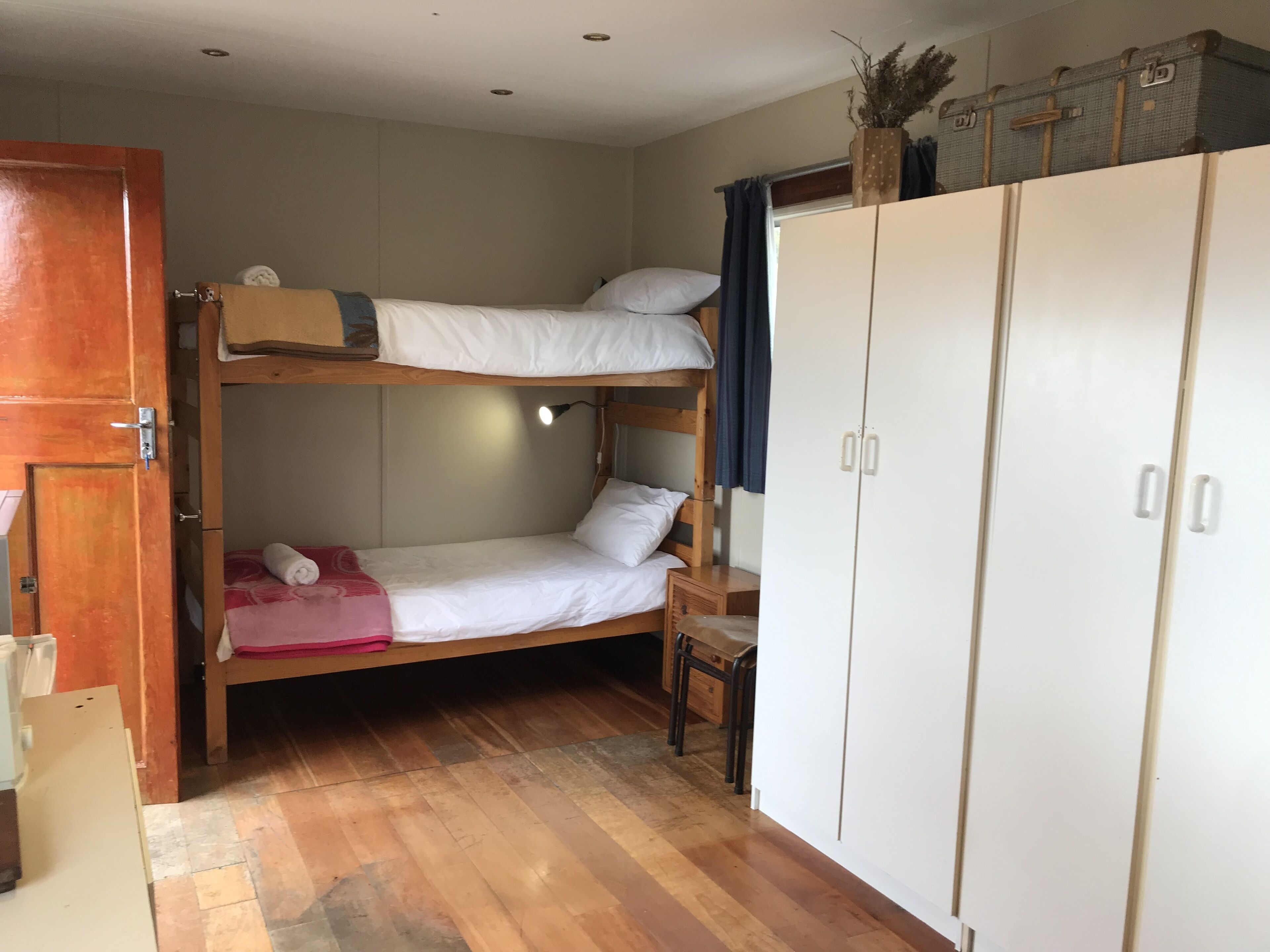 Habitación con literas, suelo de madera, armario y una mesita.