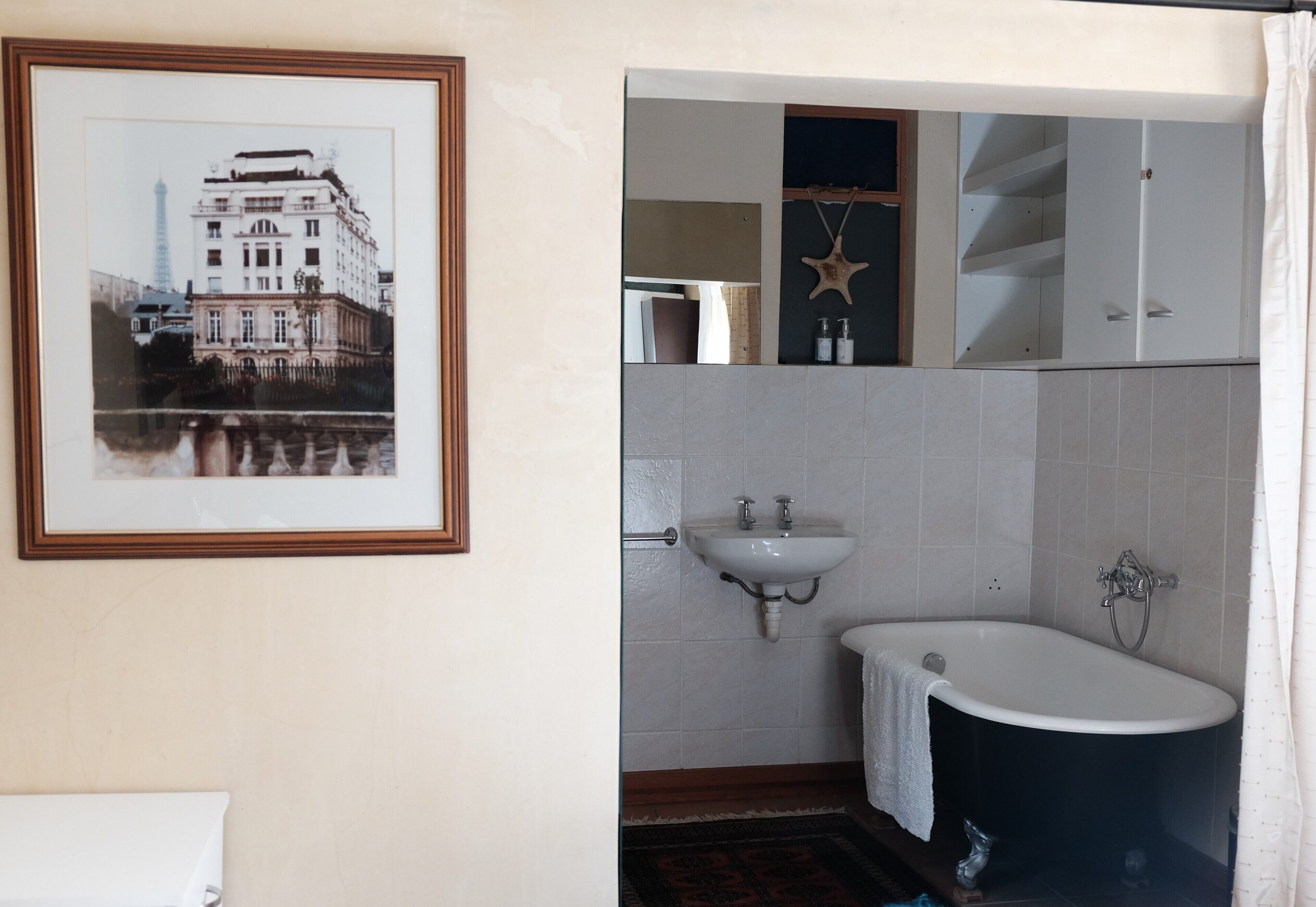 A bathroom with a framed photograph, a sink, a bathtub, and a mirror.