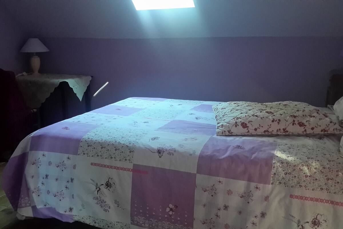 Een slaapkamer met een bed, nachtkastje, lamp en raam.