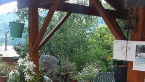 Une terrasse extérieure avec un sol en pierre, une pergola en bois, des plantes en pot, une table avec des chaises et un panneau indicateur.