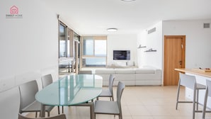 Ein modernes Wohnzimmer mit einem Glastisch, grauen Stühlen, einem weißen Sofa, einer Holztür und einem Fernseher an der Wand.