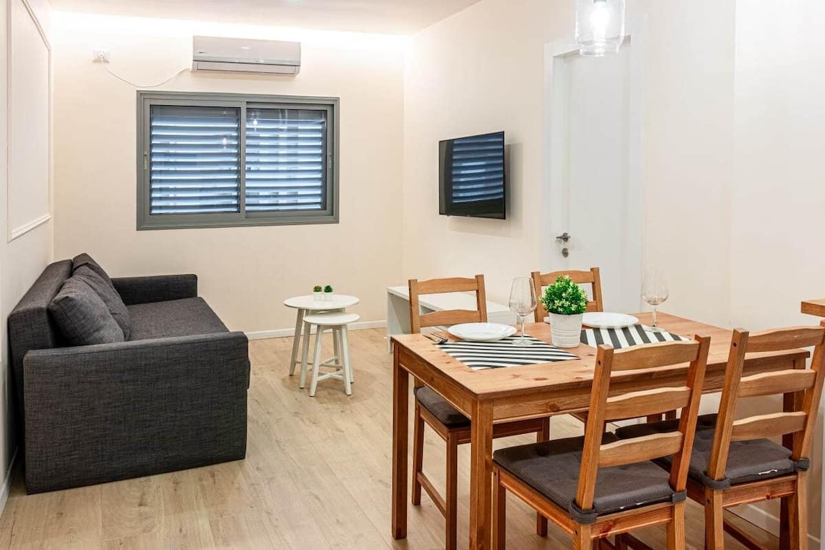 A compact living space with a sofa, a dining table set for two, a small side table, and a TV mounted on the wall.