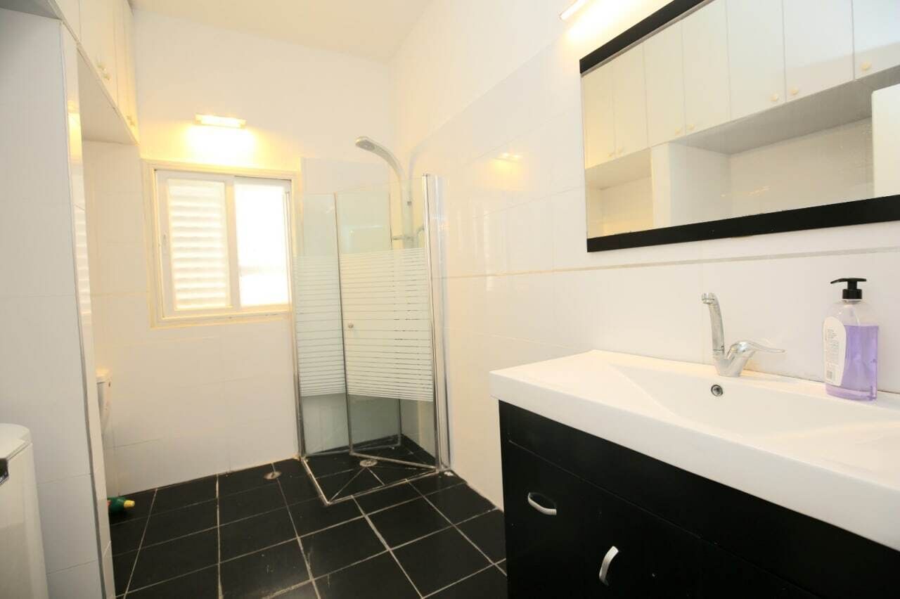 A bathroom with a white sink, black cabinet, and a glass shower enclosure.