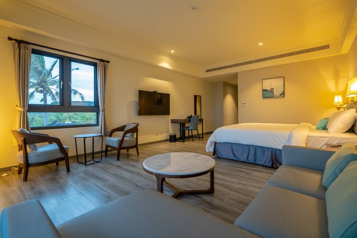A hotel room with a bed, a sofa, a round table, a desk, and a TV.